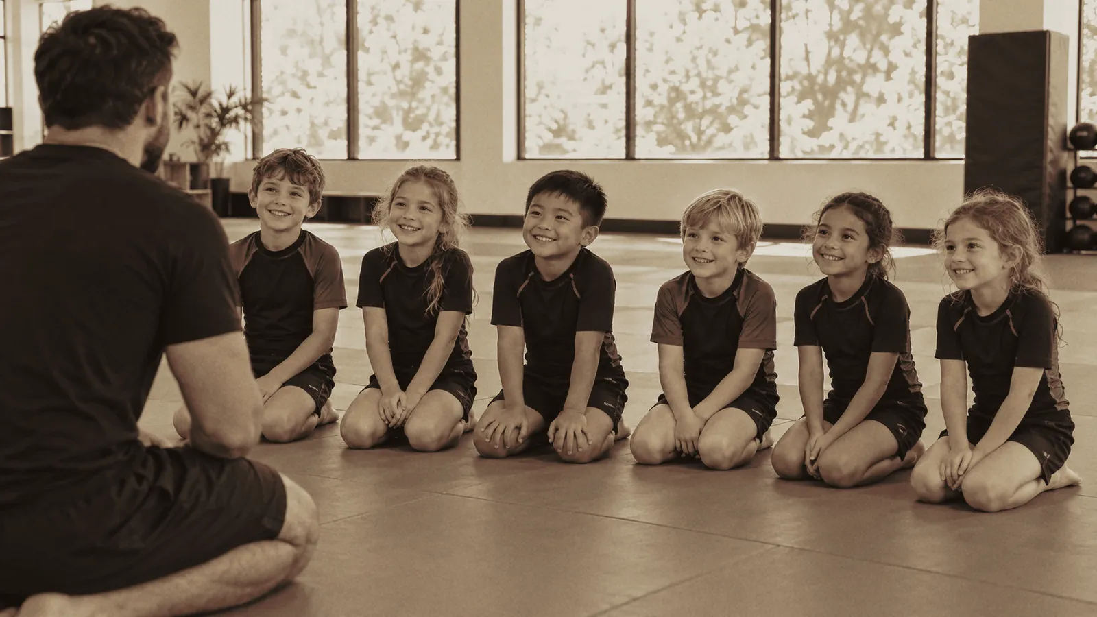 Kindertraining ohne Gi: Kinder in Rashguards knien lachend auf der Matte (Symbolbild).